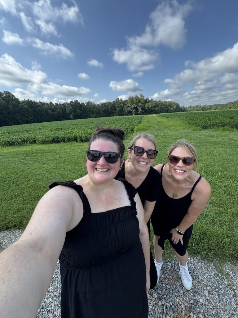 The Lael Florals crew, three women, smiling and wearing sunglasses in a sunny green field.